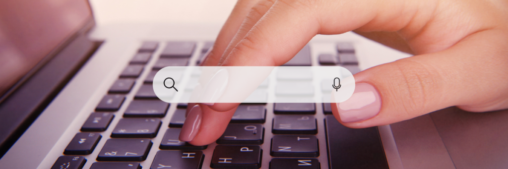 A close up of a hand typing on a laptop with a transparent search bar laid on top.
